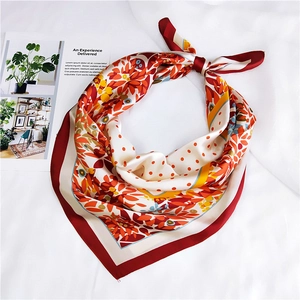 Gros plan d'un foulard carré en soie noué avec motifs floraux et pois aux tons chauds rouges