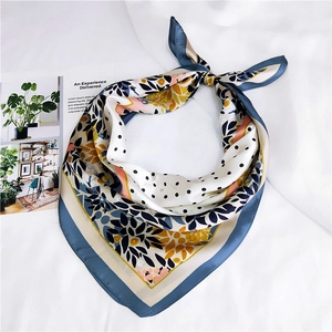 Détail d'un foulard carré en soie à fleurs et pois avec bordure bleue sur tissu blanc