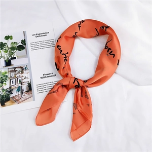 Close-up of a vibrant orange silk scarf with black cursive letters and Eiffel Tower print