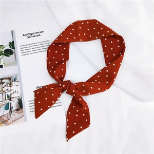 Détail d'un foulard en soie rouge à pois noué en nœud sur un magazine et du tissu blanc