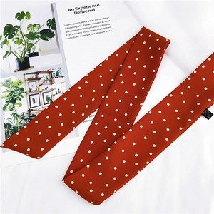 Gros plan d'un foulard en soie marron rouge à pois posé sur une surface blanche