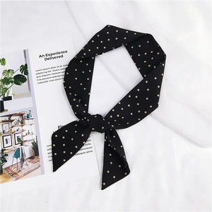 Gros plan d'un foulard en soie noir à pois noué sur un fond de tissu blanc