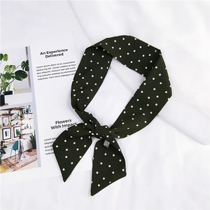 Gros plan d'un foulard en soie à pois vert foncé noué en nœud sur fond texturé blanc