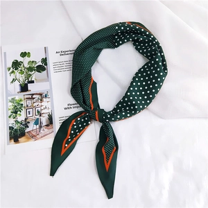 Close-up of dark green silk scarf with white polka dots and orange edge on white fabric