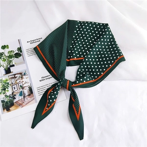 Close-up of silk scarf with dark green polka dots and vibrant orange border detailing