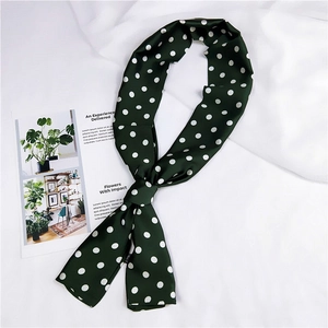 Dettaglio della sciarpa in seta verde scuro a pois drappeggiata su un tessuto bianco