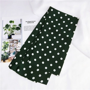 Dettaglio di una sciarpa di seta a pois verde scuro su uno sfondo di tessuto bianco pulito