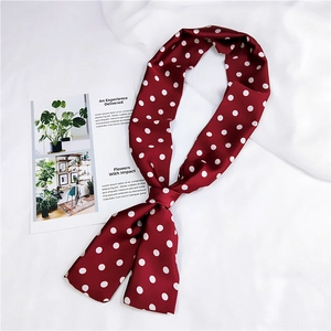 Dettaglio di un lungo foulard di seta bordeaux a pois su uno sfondo di tessuto bianco