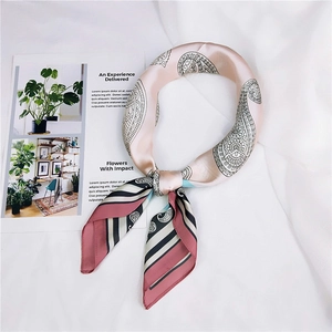 Détail d'un foulard en soie rose avec motifs paisley et rayures sur un fond blanc épuré