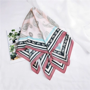 Détail d'un foulard carré en soie rose clair avec motif paisley et bordure géométrique