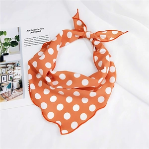 Detail of bright orange silk scarf with white polka dots folded in a bow on textured fabric