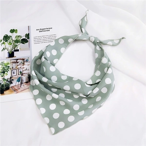 Detail of light green polka dot silk neck scarf tied in a bow over lifestyle background