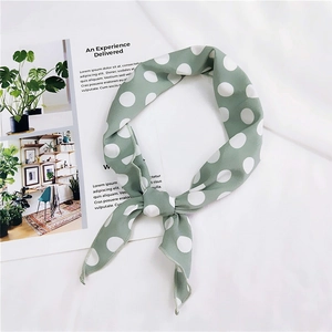 Detail of a dusty green silk scarf with white polka dots tied in a knot on a white fabric