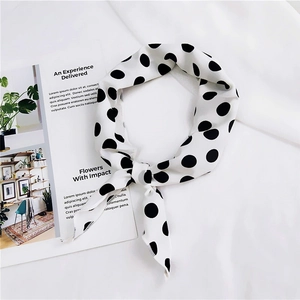 Close-up of white silk scarf with black polka dots styled with a knot on a white textile