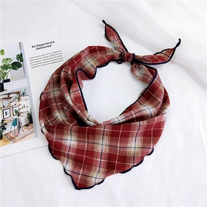Detailed view of a red plaid neck scarf with blue wavy stitched edges on a white background