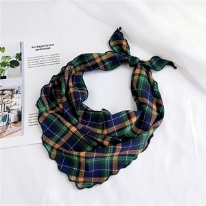 Detail of multi-color plaid triangle scarf with unique scalloped edges on white fabric