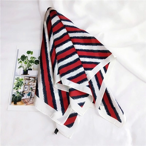 Close-up of a striped silk scarf with red, navy, and white patterns on a white background