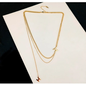 Dettaglio della collana dorata a doppio strato con pendente a lettera H e nappine