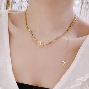 Collana doppia dorata con catena a maglie e ciondoli a forma di lettera H