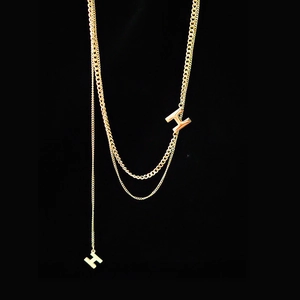 Dettaglio collana dorata multistrato con pendenti a forma di H su catenine sottili