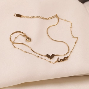 Detail of double-layer gold anklet with heart and love charms on textured fabric