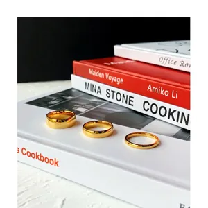 Three minimalist gold titanium steel rings of varying widths on white books