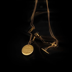 Layered gold chain necklace with toggle clasp and engraved round pendant on black leather