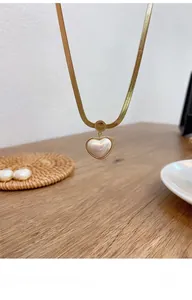 Detail of gold snake chain with heart pendant and Love engraved charm on wood