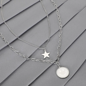 Silver layered necklace featuring star and smiley pendants on a textured grey fabric backdrop