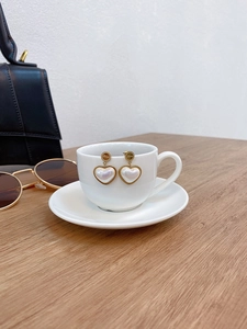Elegant gold heart earrings with pearl finish and Love engraving on a coffee cup