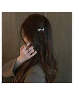 Detail of elegant leaf hair clip with shiny zircons and a pearl on brown wavy hair