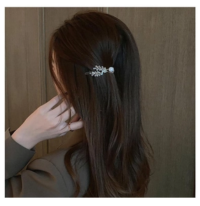 Detail of silver leaf hair clip with zircon and pearl on a textured wooden background