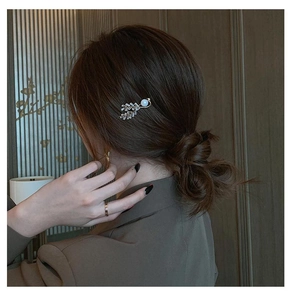 Close-up of golden leaf hair clip with zircon and pearl on a side-swept bun