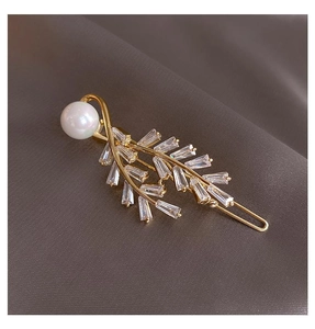 Detailed view of leaf hair clip with shiny zircons and white pearl on silk background