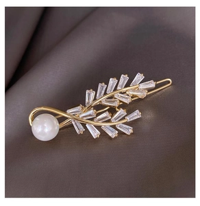 Detail shot of golden leaf hair clip with zircon studs and a single white pearl accent