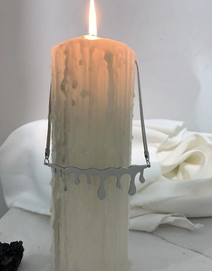 Artistic detail of silver liquid melt pendant necklace draped on a melting wax candle
