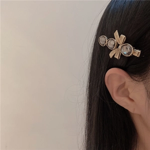 Dettaglio del fermaglio vintage con cristalli grigi e fiocco dorato sui capelli neri
