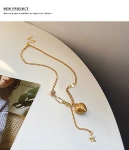 Dettaglio della collana dorata con ciondoli a cuore e stella su marmo bianco