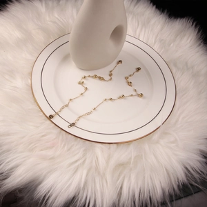 Polished gold stainless steel bead anklet with lobster clasp on white ceramic plate