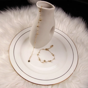 Polished gold beaded anklet and bracelet set with lobster clasp on elegant white background