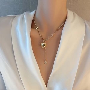 Collana dorata con ciondoli a cuore e stella indossata su una camicia di seta bianca