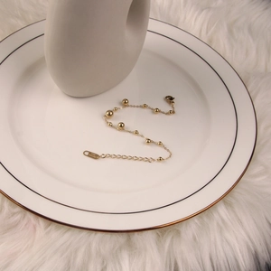Minimalist gold stainless steel beaded anklet featuring a lobster clasp on a ceramic plate