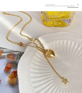 Dettaglio della collana a strati dorata con ciondoli a cuore e stella su piatto ceramico