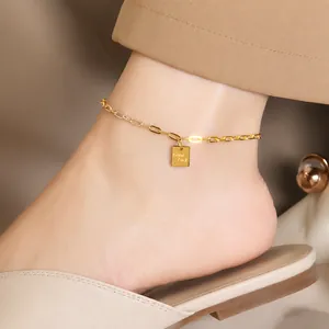 Detail eines 18K Gold-Fußkettchens mit quadratischem Good Luck Anhänger zu Sandalen