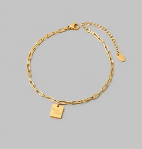 Detail der goldenen Büroklammer-Fußkette mit quadratischem Good Luck Gravuranhänger