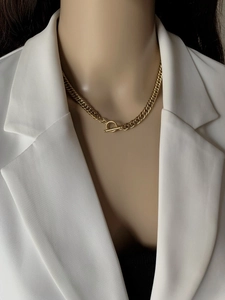 Detailed close-up of golden Cuban link necklace with T-bar toggle clasp on white blazer