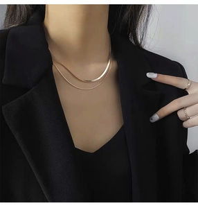 Detail of layered gold flat snake chain and bead necklace on a model in black suit