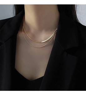 Close-up of double-layered gold snake chain and beaded necklace on a black blazer