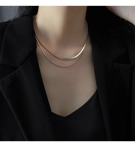 Detail of layered gold snake chain and beaded necklace on a model wearing black
