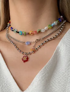 Détail d'un ensemble de colliers superposés avec pendentif fleur rouge et perles